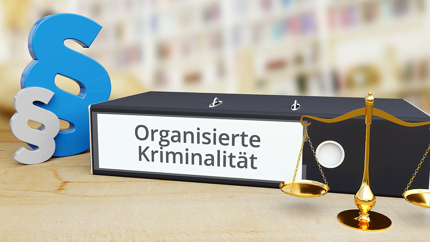 Organisierte Kriminalität – Recht/Gesetz. Ordner auf Schreibtisch mit Beschriftung neben Paragraf und Waage. Anwalt Organisierte Kriminalität – Recht/Gesetz. Ordner auf Schreibtisch mit Beschriftung neben Paragraf und Waage. Anwalt