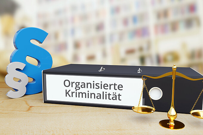 Organisierte Kriminalität – Recht/Gesetz. Ordner auf Schreibtisch mit Beschriftung neben Paragraf und Waage. Anwalt Organisierte Kriminalität – Recht/Gesetz. Ordner auf Schreibtisch mit Beschriftung neben Paragraf und Waage. Anwalt