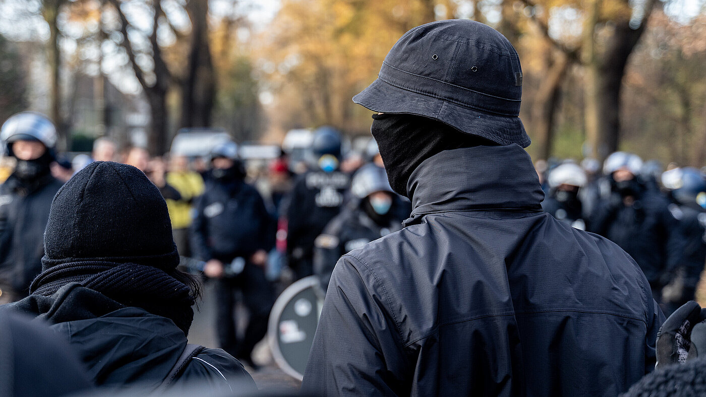 Anonymous masked left wing antifa, or so called black block is standing in front of a riot police line with helmets on in Germany to block other protesters.